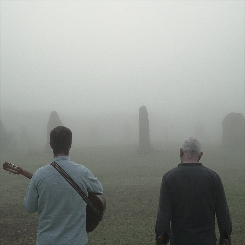 two people, possibly mitchell and vincent, stand in a mysterious and misty landscape